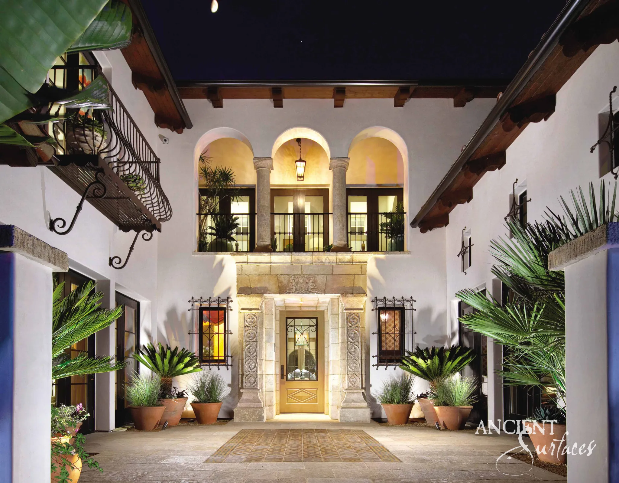 Reclaimed antique limestone entryway from Ancient Surfaces photographed at night beneath a two storey arched loggia in a lit courtyard