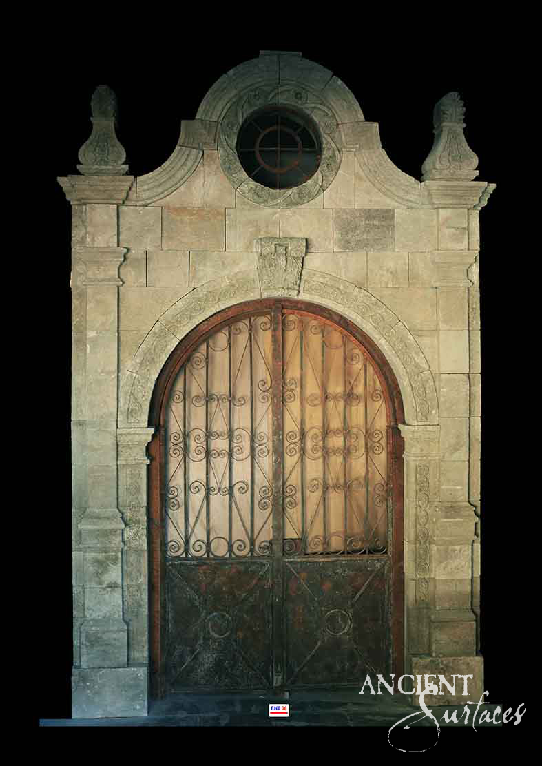 Reclaimed antique limestone entryway from Ancient Surfaces with a broken scrolled pediment, carved finials and a round oculus window above an arched wrought iron gate