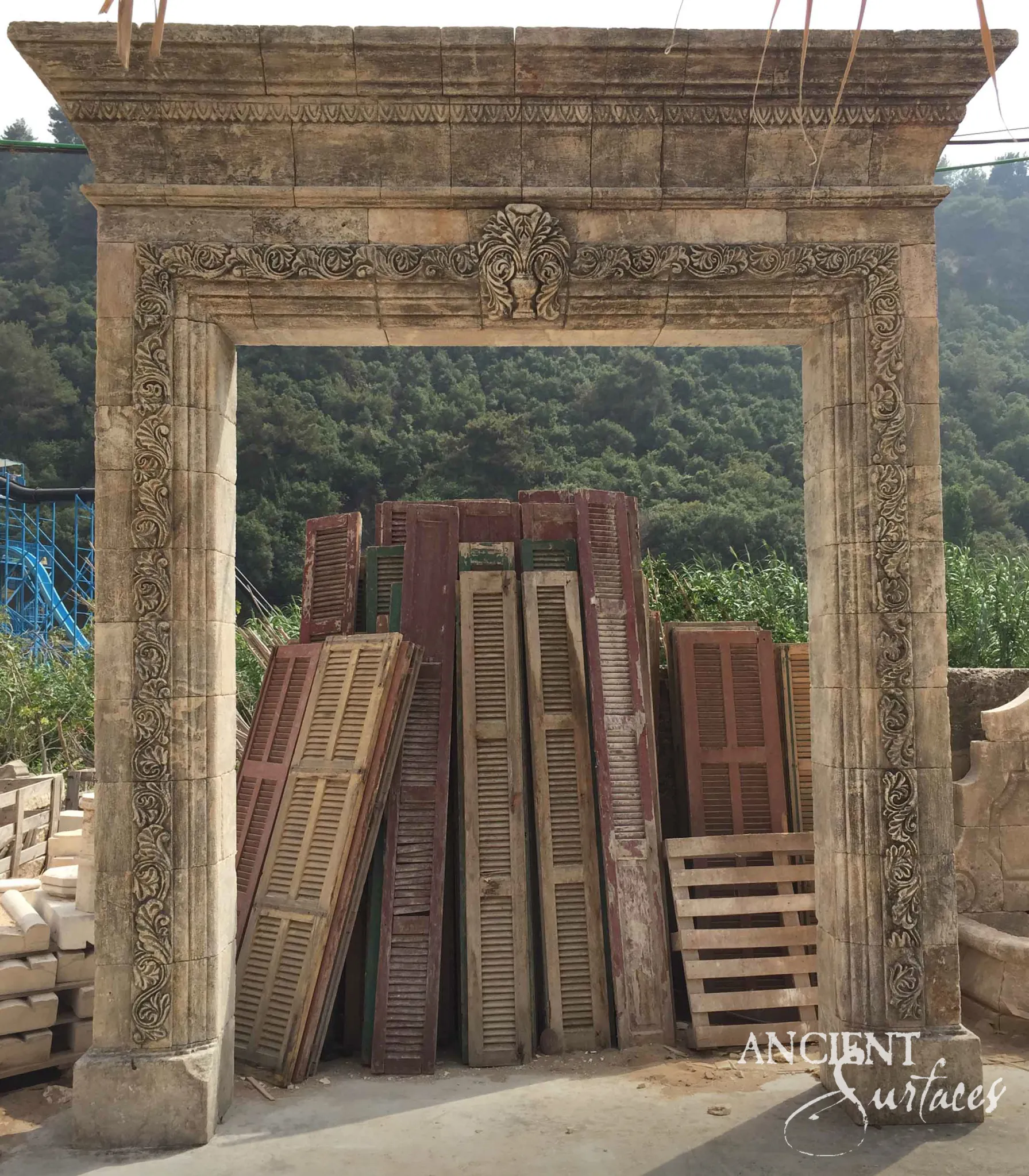 Reclaimed antique limestone entryway from Ancient Surfaces densely carved with scrolling acanthus around the jambs and lintel, photographed in the stoneyard with rigging straps still in place