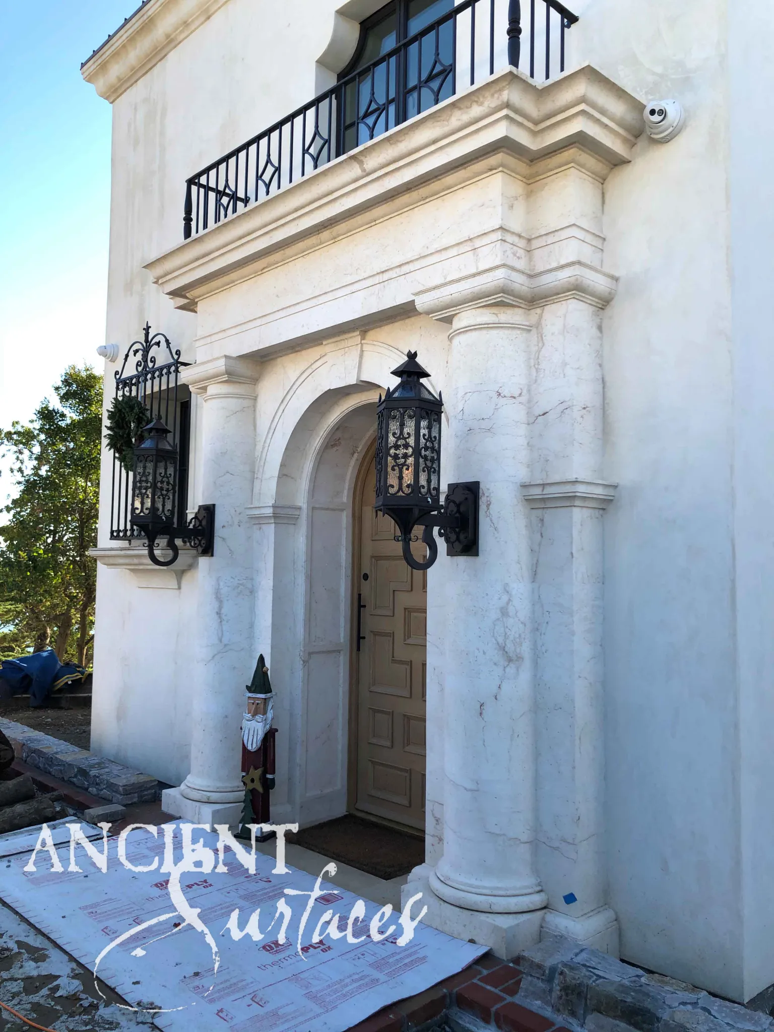 Reclaimed antique limestone entryway from Ancient Surfaces with tall veined pilasters rising to a wrought iron balcony on a two storey stucco facade