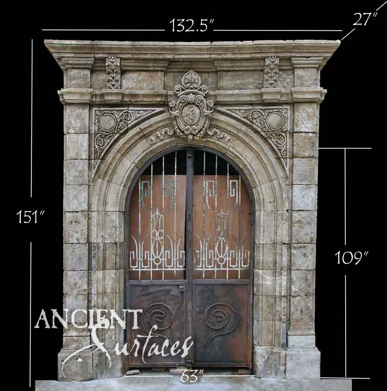 Grand reclaimed antique limestone entryway from Ancient Surfaces with a carved crest spandrel, fleur finial and geometric wrought iron gate, photographed against black with dealer measurements