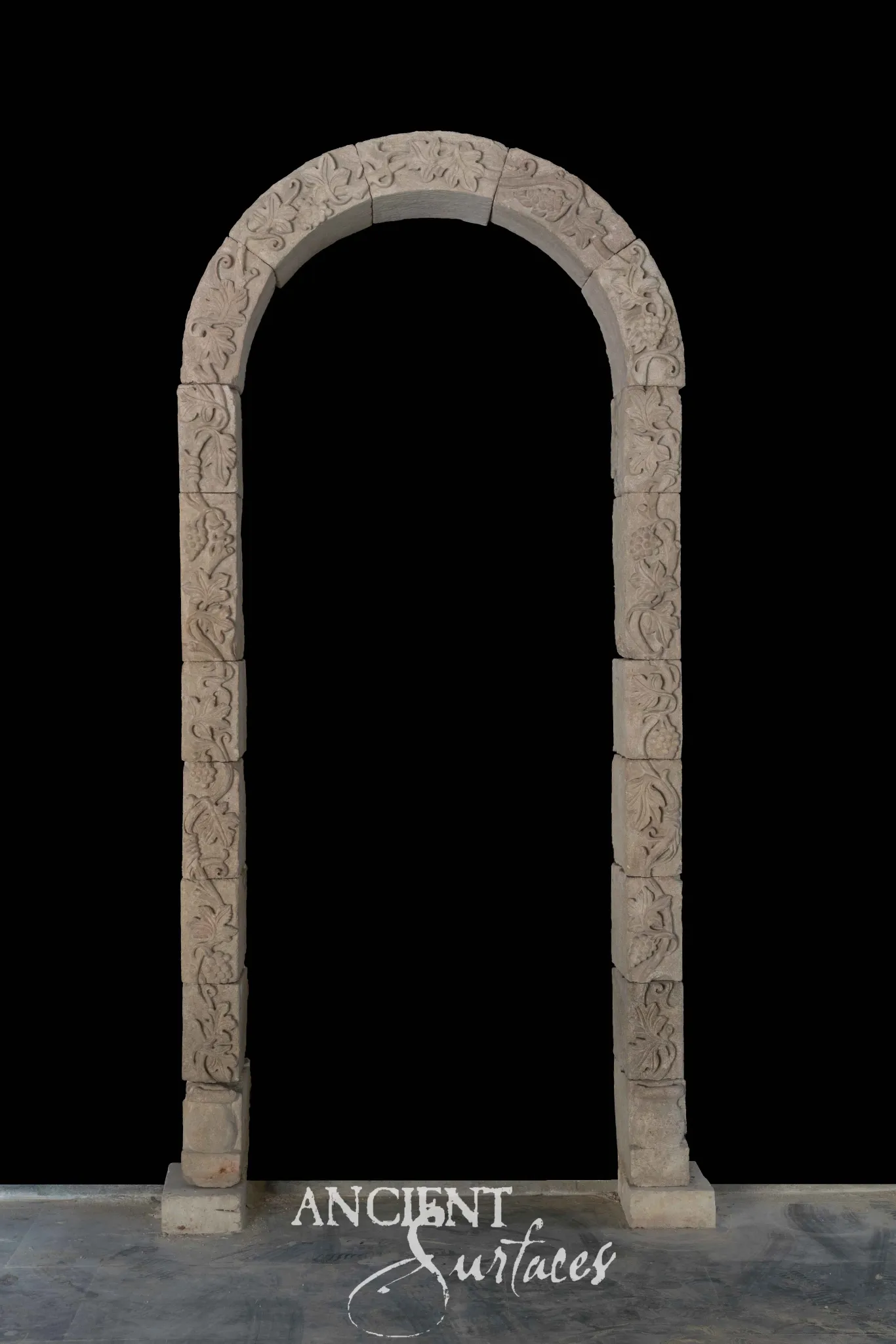 Reclaimed antique limestone entryway from Ancient Surfaces, a bare continuous arch carved with running vine scrollwork on plain square jambs, photographed against black