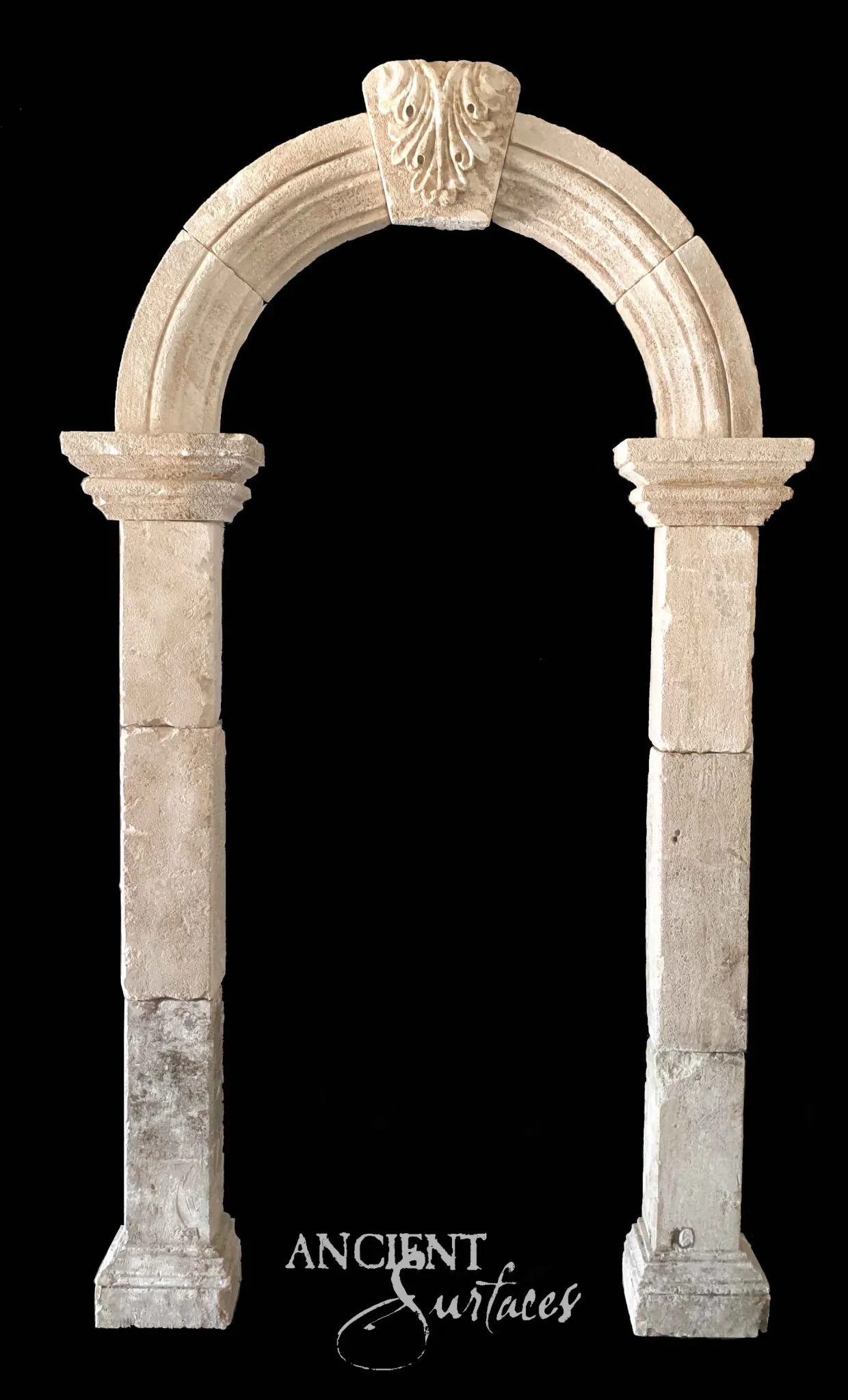 Reclaimed antique limestone entryway from Ancient Surfaces with round column like jambs and a plain arch, showing genuine two tone weathering, photographed against black