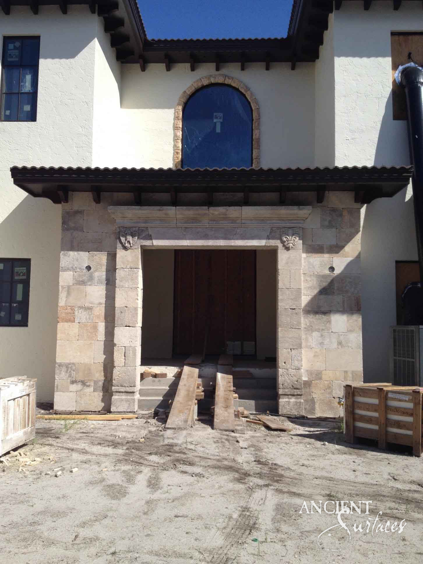 Reclaimed antique limestone entryway from Ancient Surfaces with carved scroll brackets, photographed mid installation on a Tuscan style villa with shipping crates in the yard