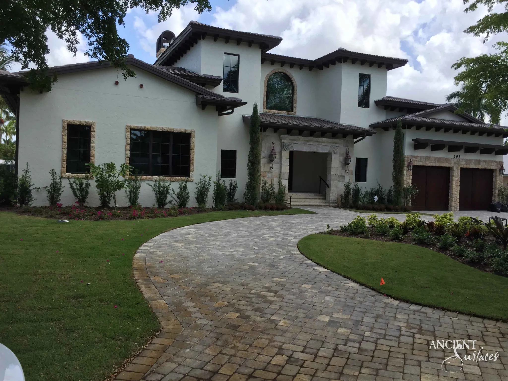 Reclaimed antique limestone entryway from Ancient Surfaces set into a pale stucco Mediterranean estate facade, photographed from across a curved paver driveway